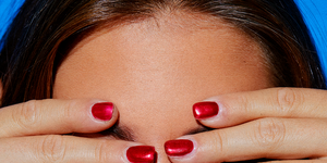 a woman with red fingernails covering her eyes and biting her lip
