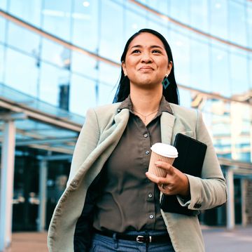 confident businesswoman walking outside office building holding coffee and tablet