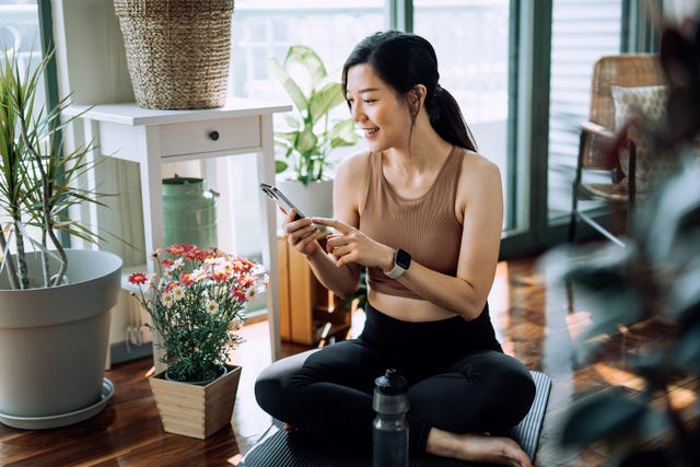 confident fitness young asian woman relaxing after exercising at home young asian female in sports wear scrolling on smartphone and resting after home work out fitness training with technology health, fitness and wellness concept