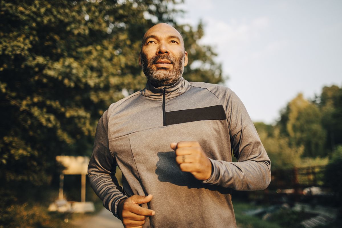 confident man looking away while jogging in park during sunset