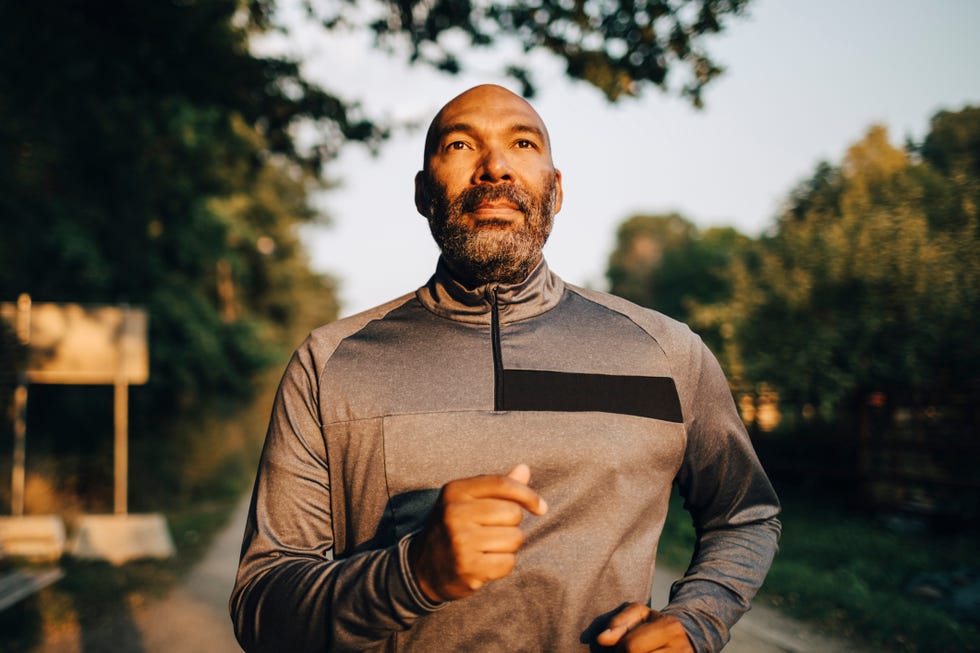 confident mature man looking away while jogging in park during sunset
