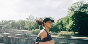 Confident sportswoman listening music through in-ear headphones while jogging on bridge in city