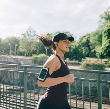 confident sportswoman listening music through in ear headphones while jogging on bridge in city