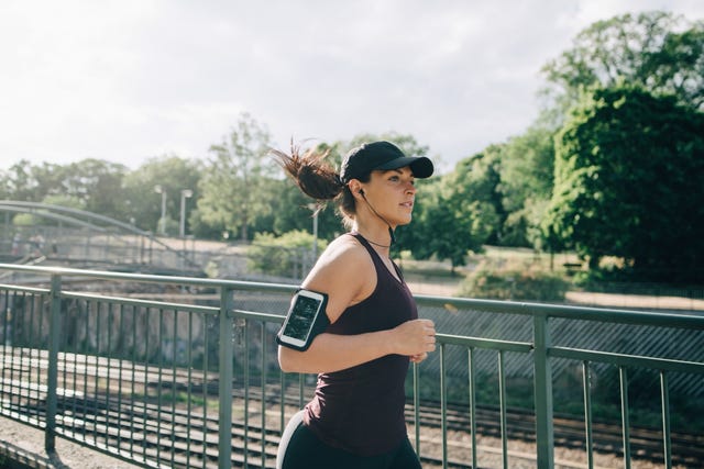 confident sportswoman listening music through in ear headphones while jogging on bridge in city