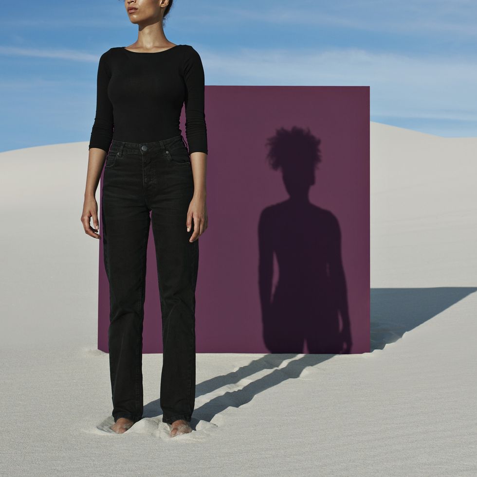 confident young fashion model standing against purple placard at white desert
