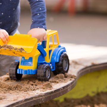 young child playing with blue and yellow construction toy and sand