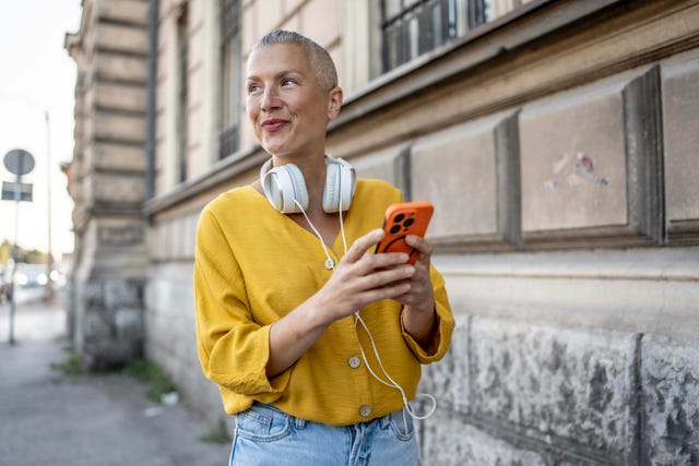 una mujer sonr´liemientras camina por la calle consultando su teléfono móvil