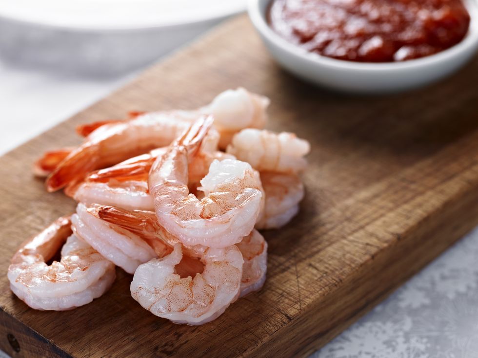 cooked shrimps on wooden board next to red sauce
