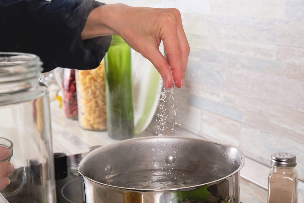 cooking italian pasta with cream sauce and basil, at home a girl or woman adds salt to boiling water next to it, raw macaroni in a glass jar vegetarian food step by step instructions, do it yourself step 2