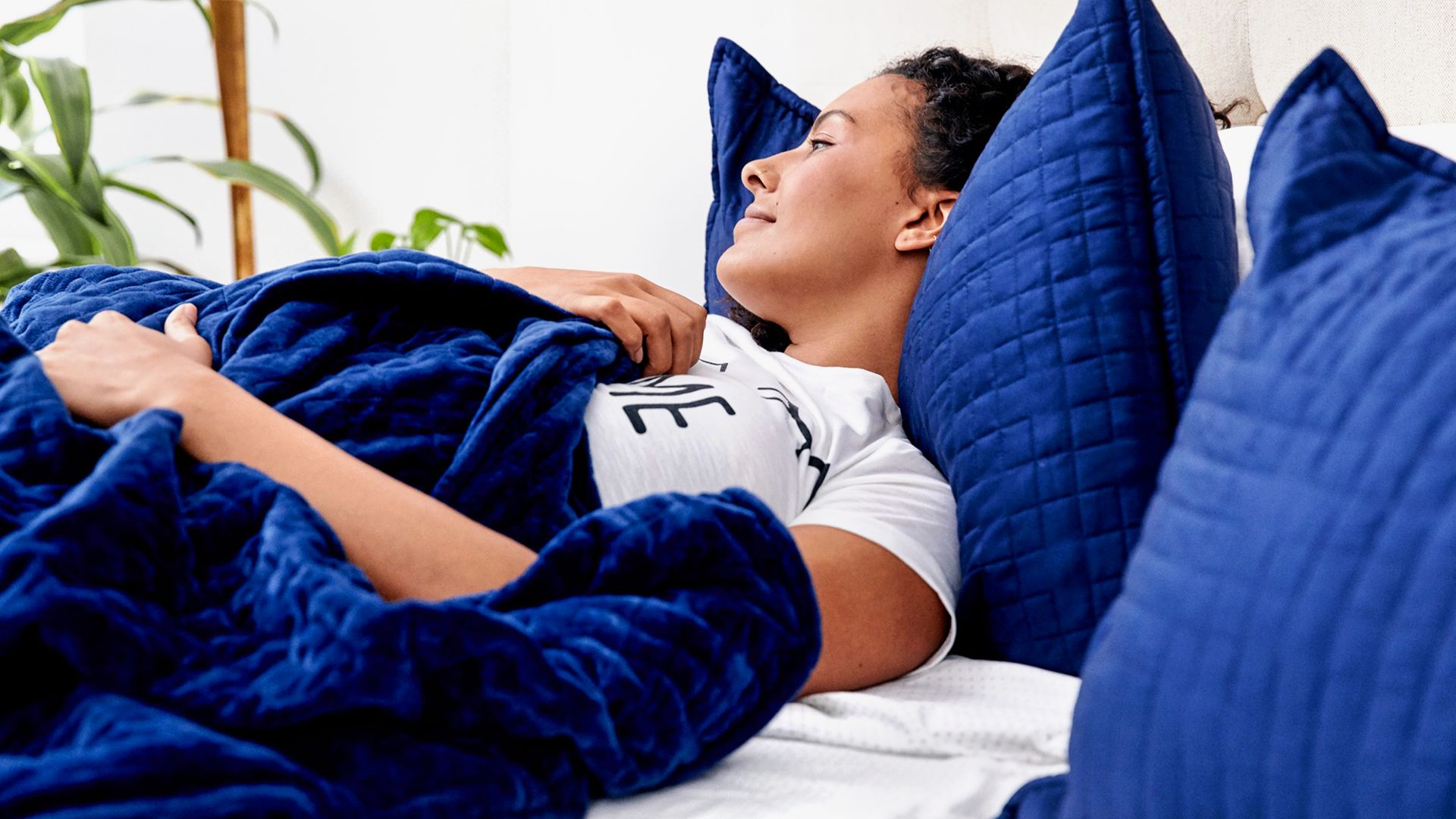 woman lying in bed with blue gravity blanket and pillows