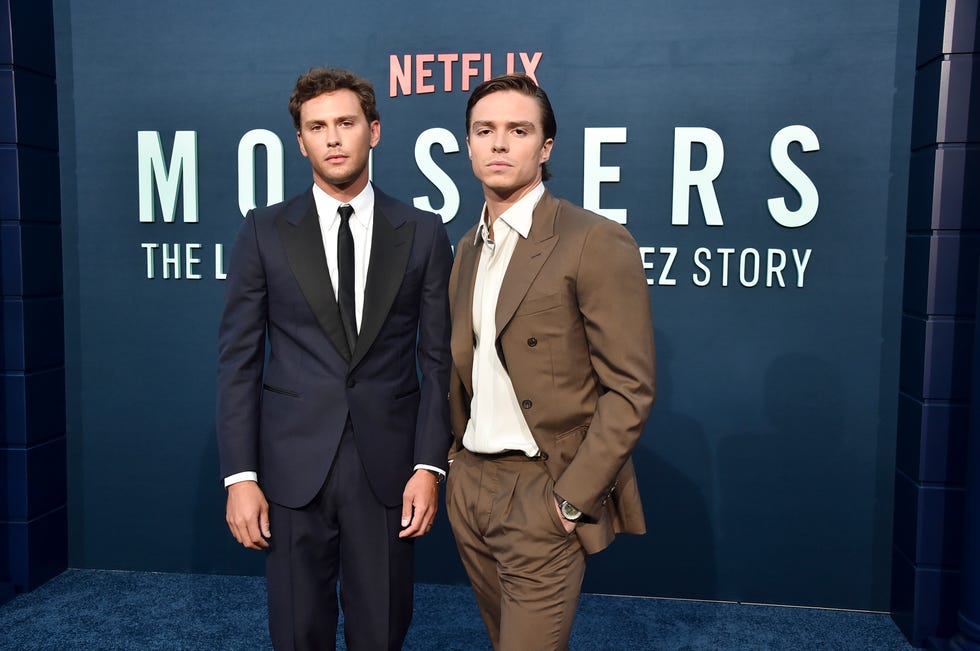 Cooper Koch and Nicholas Alexander Chavez stand next to each other in front of a Netflix set for “Monsters,” both men wearing suits and white collared shirts