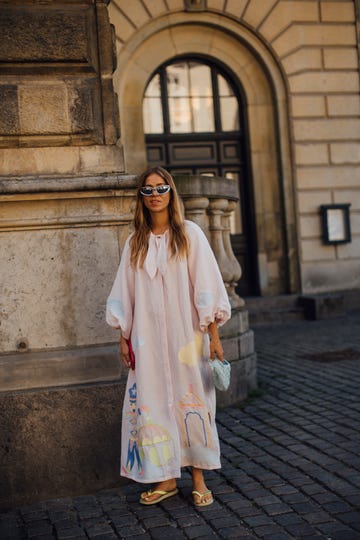 a woman wearing a white dress and sunglasses standing in front of a building