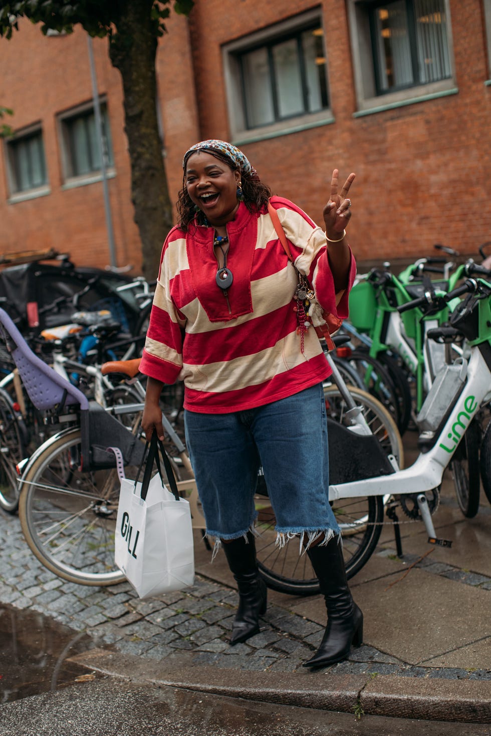 Individual posing with a peace sign while holding a shopping bag surrounded by bicycles