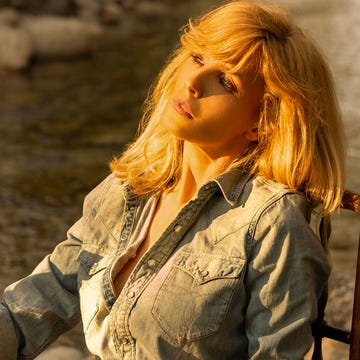 Kelly Reilly a person seated on a wooden chair by a river holding a bottle