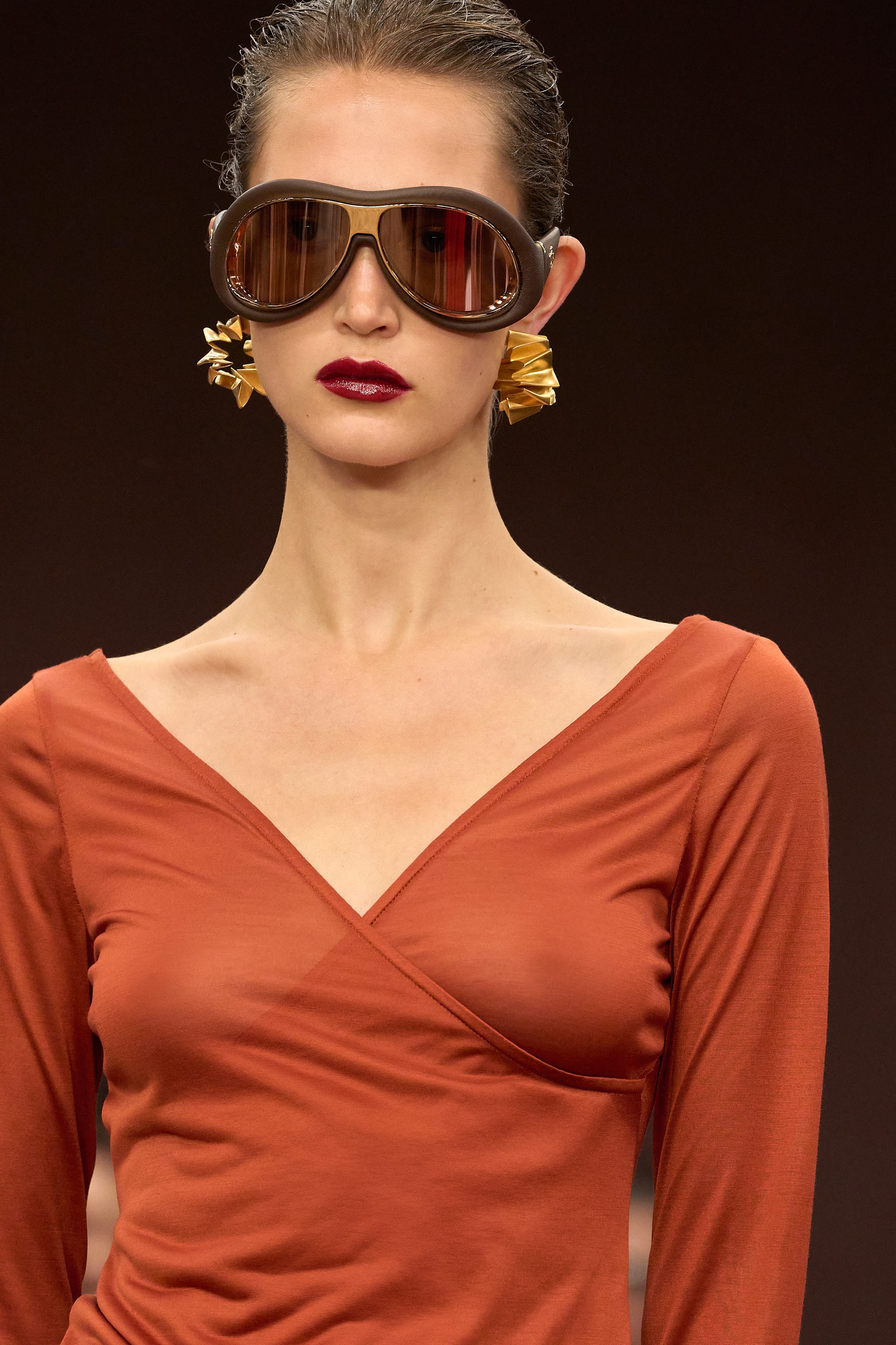 a runway model with large sunglasses wearing a red crossbody top