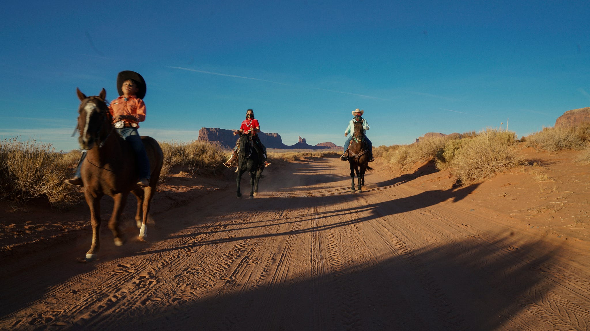 three riders on horseback walking along a dirt road in an arid landscape