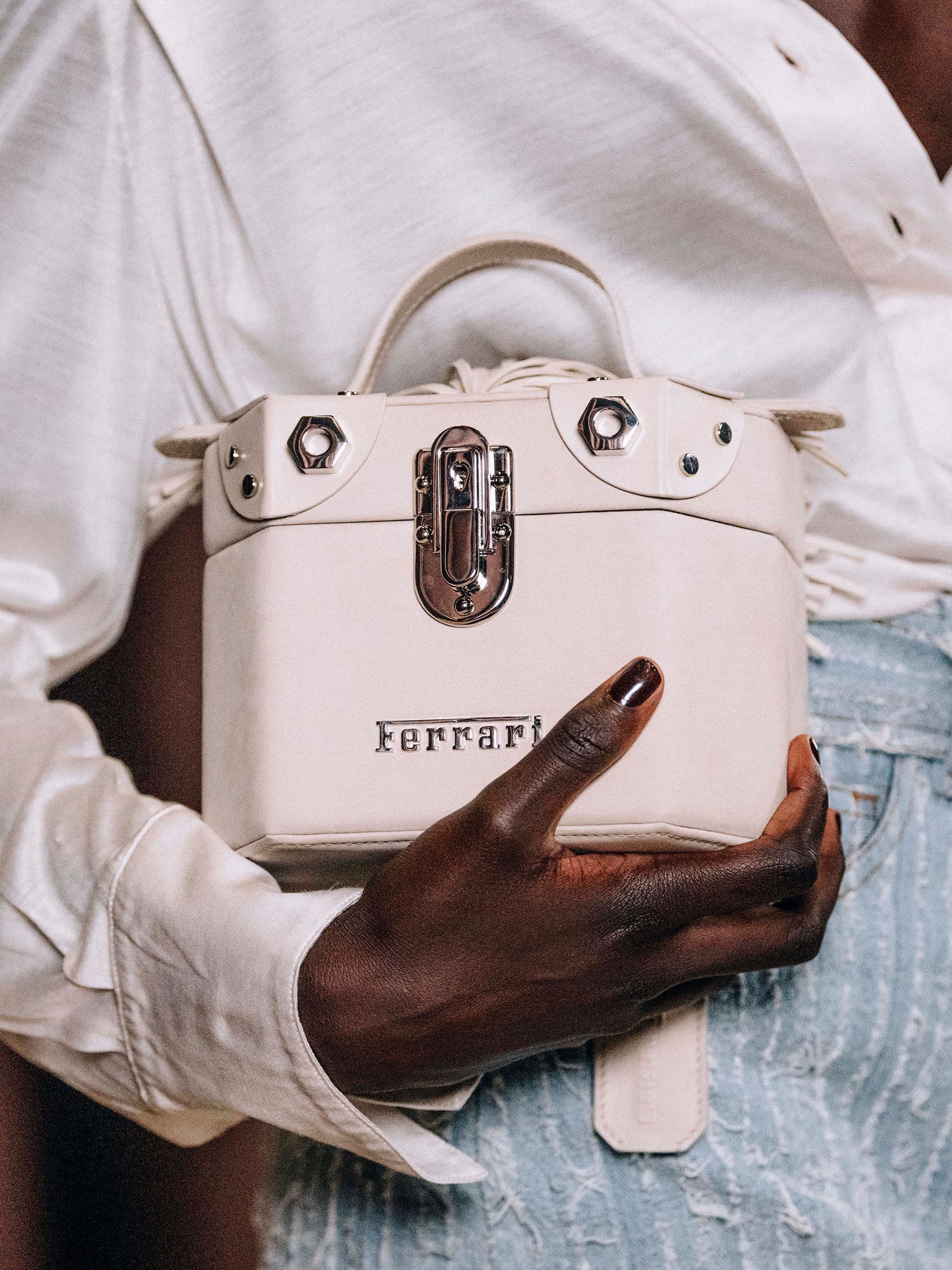 a model holds a white octagonal shaped bag with a metal ferrari logo