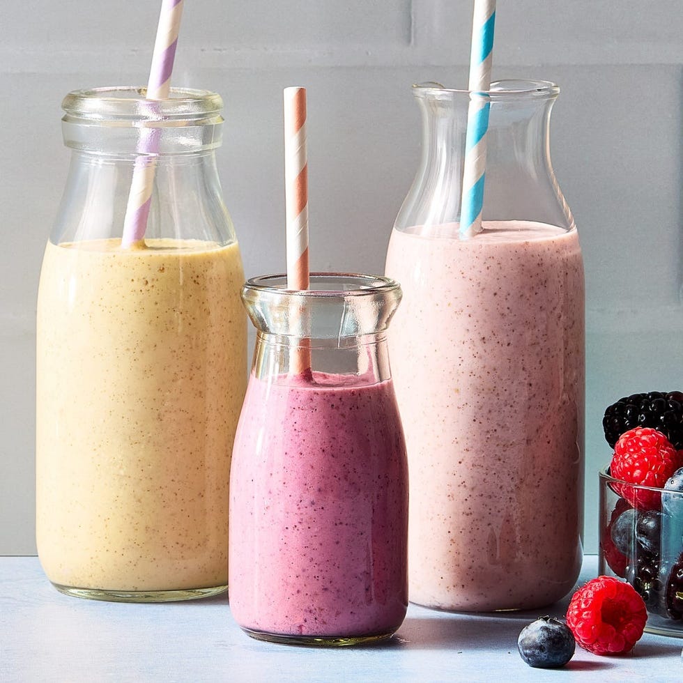 three glass bottles filled with smoothies and topped with paper straws accompanied by fresh berries