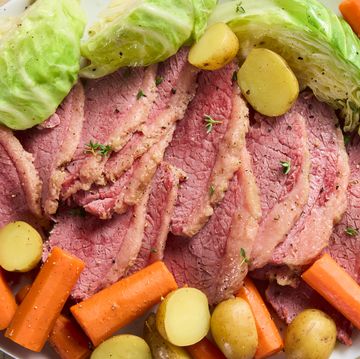 corned beef sliced on a white platter with cabbage, carrots, and sliced potatoes