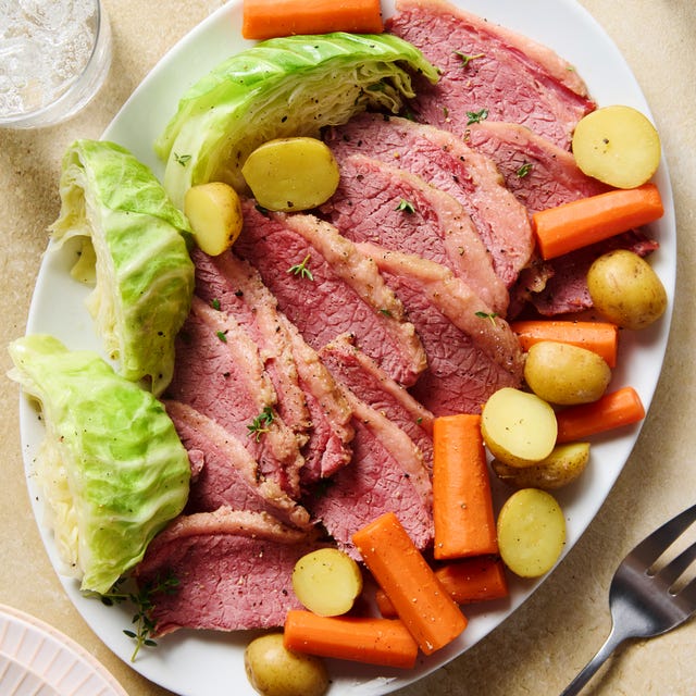 corned beef sliced on a white platter with cabbage, carrots, and sliced potatoes