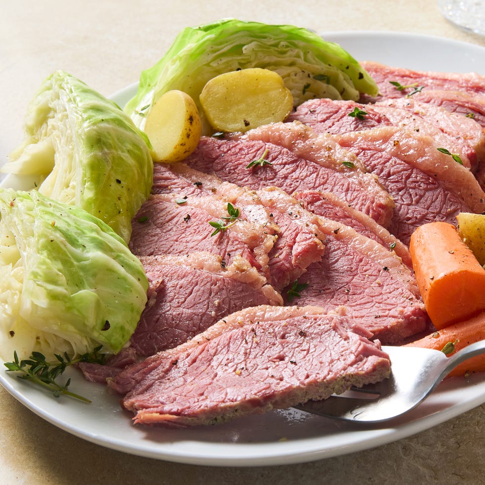 corned beef sliced on a white platter with cabbage, carrots, and sliced potatoes