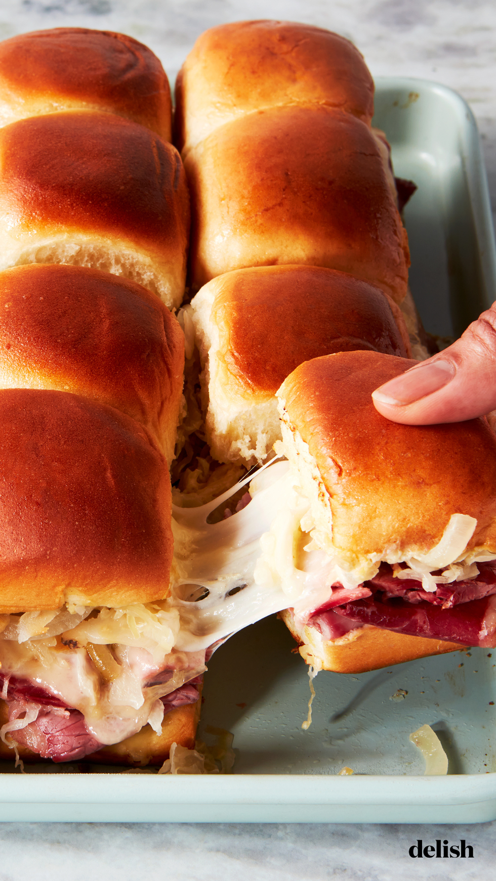 a tray of sliders made with hawaiian rolls, corned beef, sauerkraut, and swiss cheese