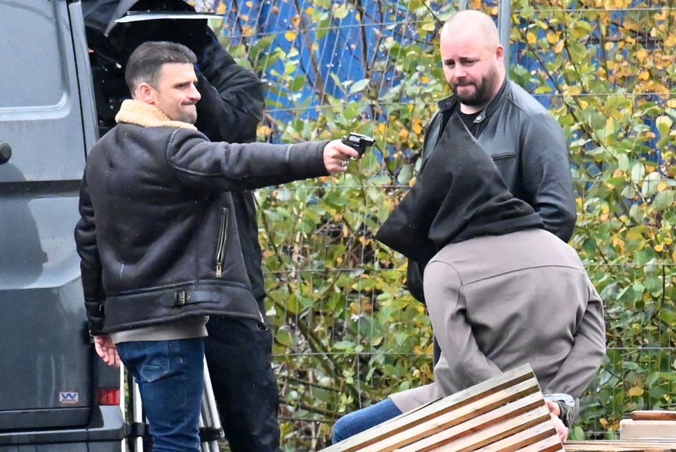 Ciaran Griffiths als Damon Hay richtet eine Waffe auf Sam Robertson als Adam Barlow, der Straßenszenen zur Krönung filmt