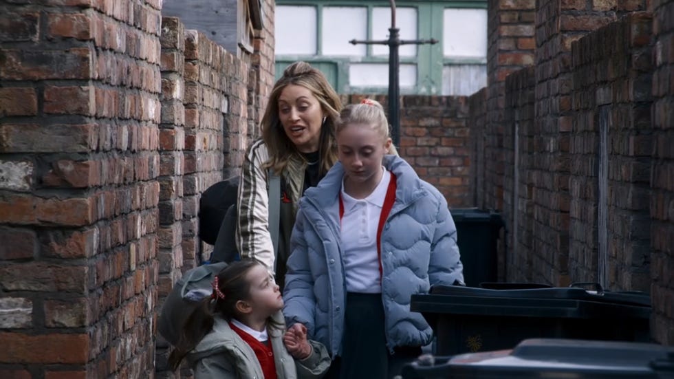 coronation street, lou, shanice, joanie all wearing puffer coats, in a narrow alleyway near brick walls and garbage bins