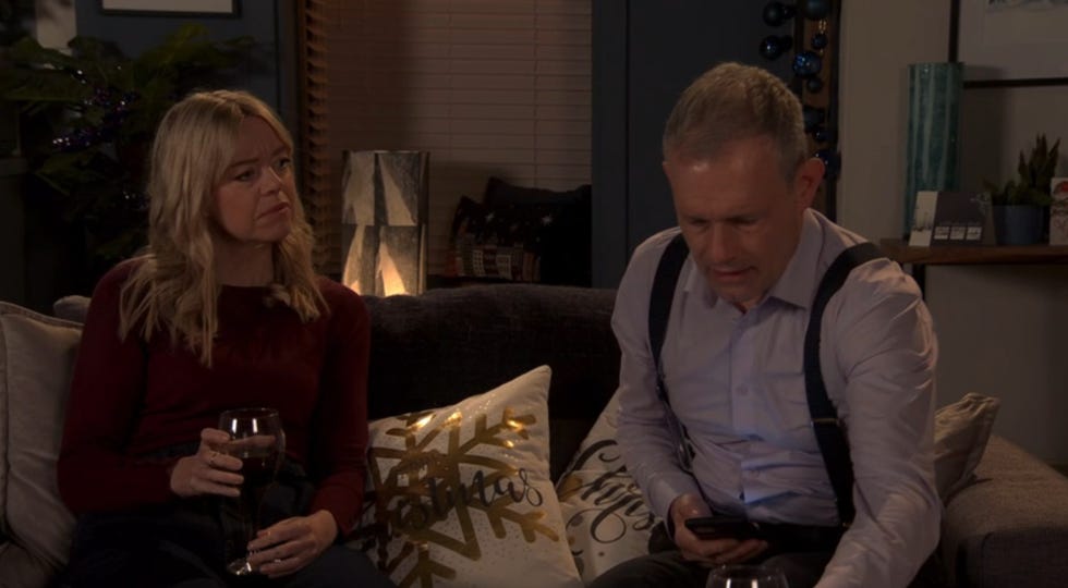 coronation street's toyah and nick talk together as they drink wine on their living room sofa