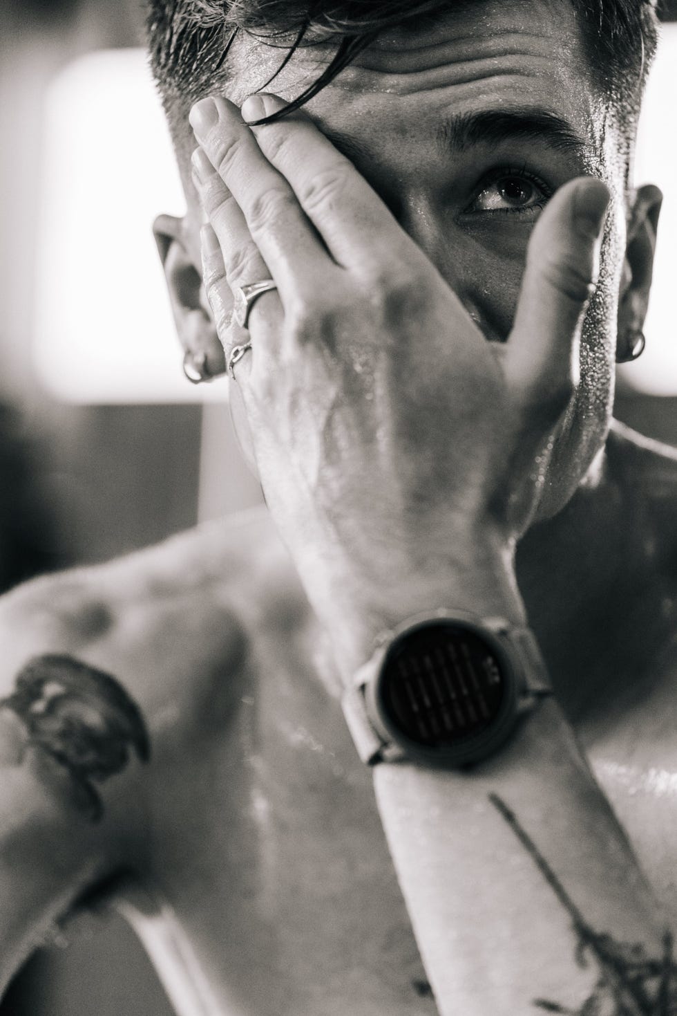 close up of a sweating man wearing a watch with his hand across part of his face