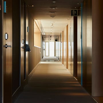 a corridor of a building where you can see several doors of rooms, it is poorly lit and in the background you can see an exit door through which most of the light enters