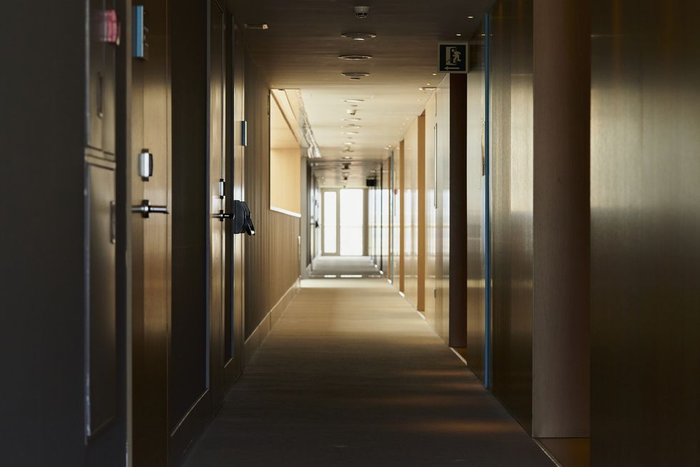 a corridor of a building where you can see several doors of rooms, it is poorly lit and in the background you can see an exit door through which most of the light enters