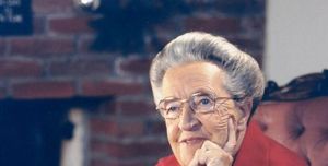 corrie ten boom sitting in a chair while resting her head in her left hand and holding a book