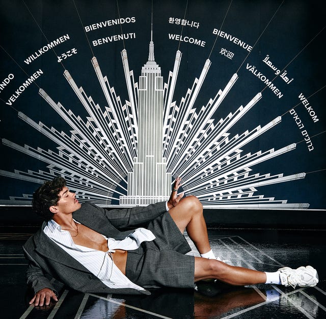 person lounged in a stylish gray suit against a wall with multiple welcome messages in different languages and an iconic building illustration person lounged in a stylish gray suit against a wall with multiple welcome messages in different languages and an iconic building illustration