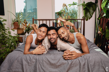 a throuple smiling in bed