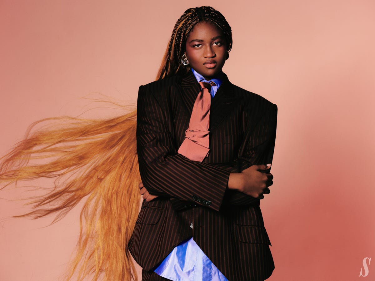 a person wearing a striped suit with a pink tie and blue shirt arms crossed