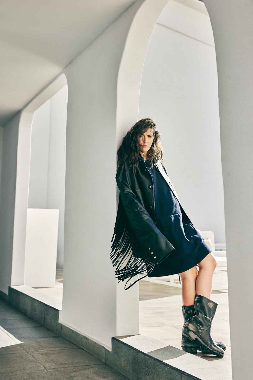 woman in fringe leather jacket and boots leaning against wall