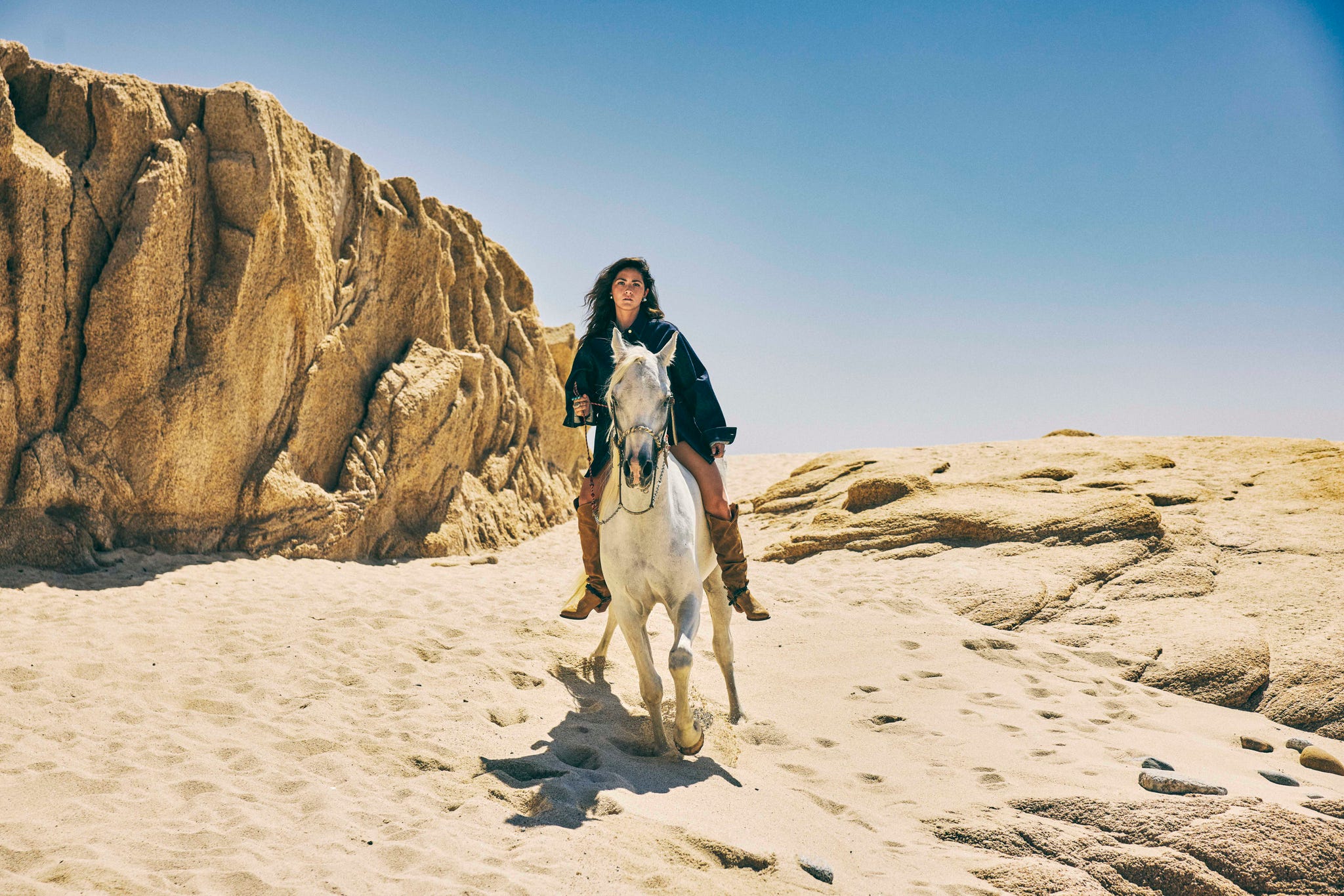 woman in denim riding horse on beach