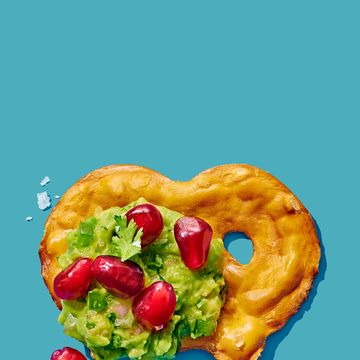 pretzel thin topped with guacamole pomegranate cilantro and flaky salt on a blue background