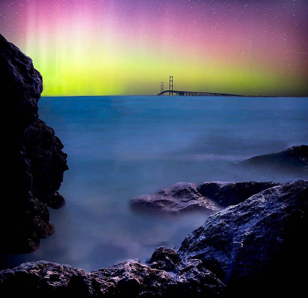 aurora borealis over a bridge and rocky shoreline