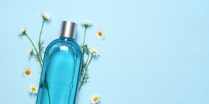 cosmetic bottle and chamomile flowers on blue table top view with text space
