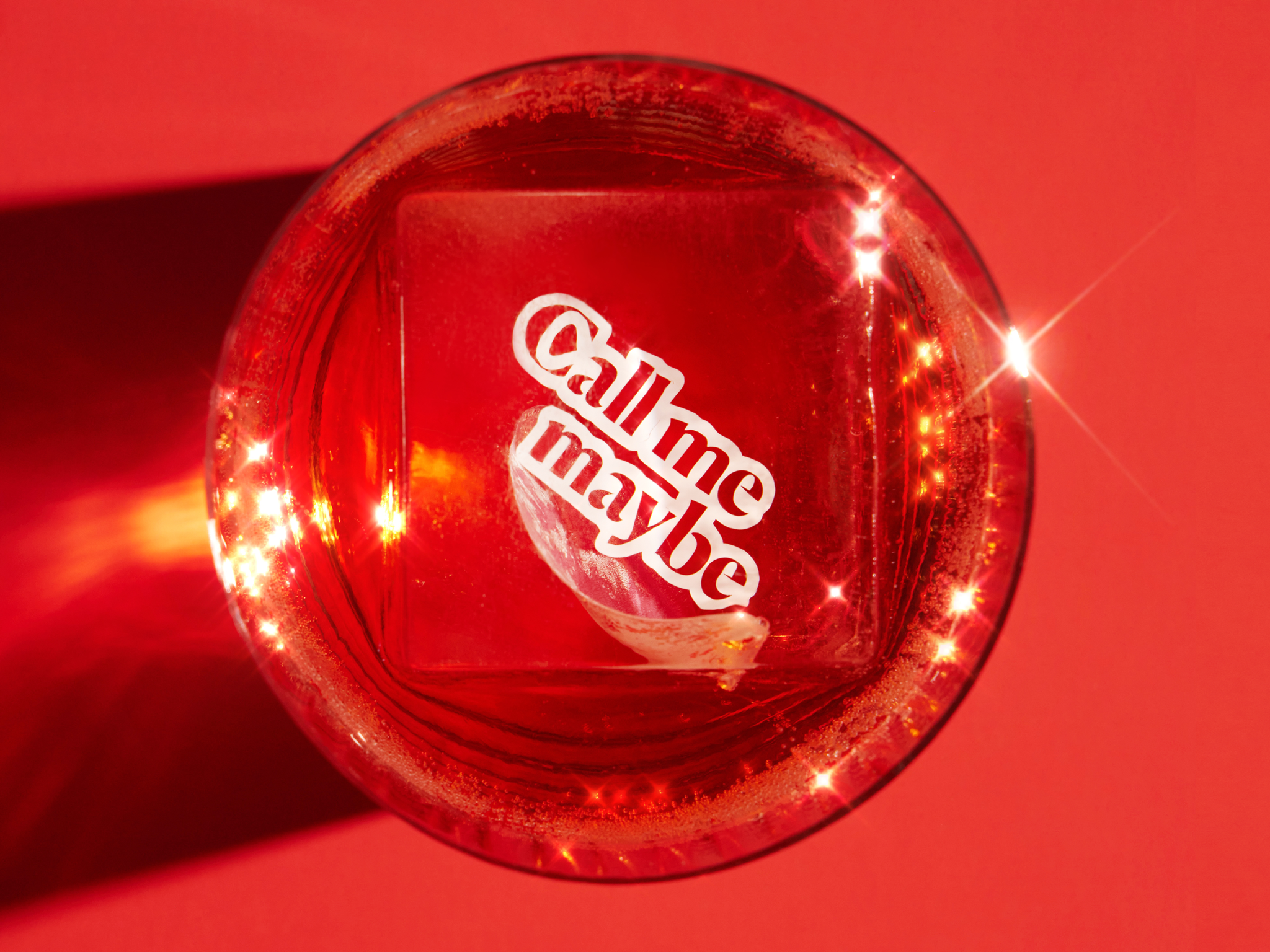 ice cube with the words "call me maybe" in a cocktail glass, shot from above on a red background