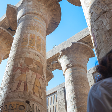 a woman stands in a temple looking up at painted pillars, with the words cosmo trips over it