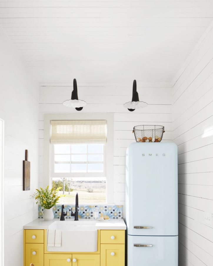 tiny white kitchen with bright yellow cabinetry and a light blue refrigerator