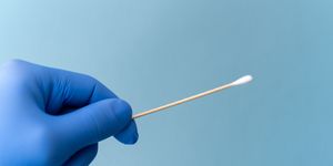 cotton swab held by hand wearing blue medical glove