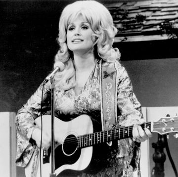 dolly parton playing guitar in front of a microphone and looking off into a crowd