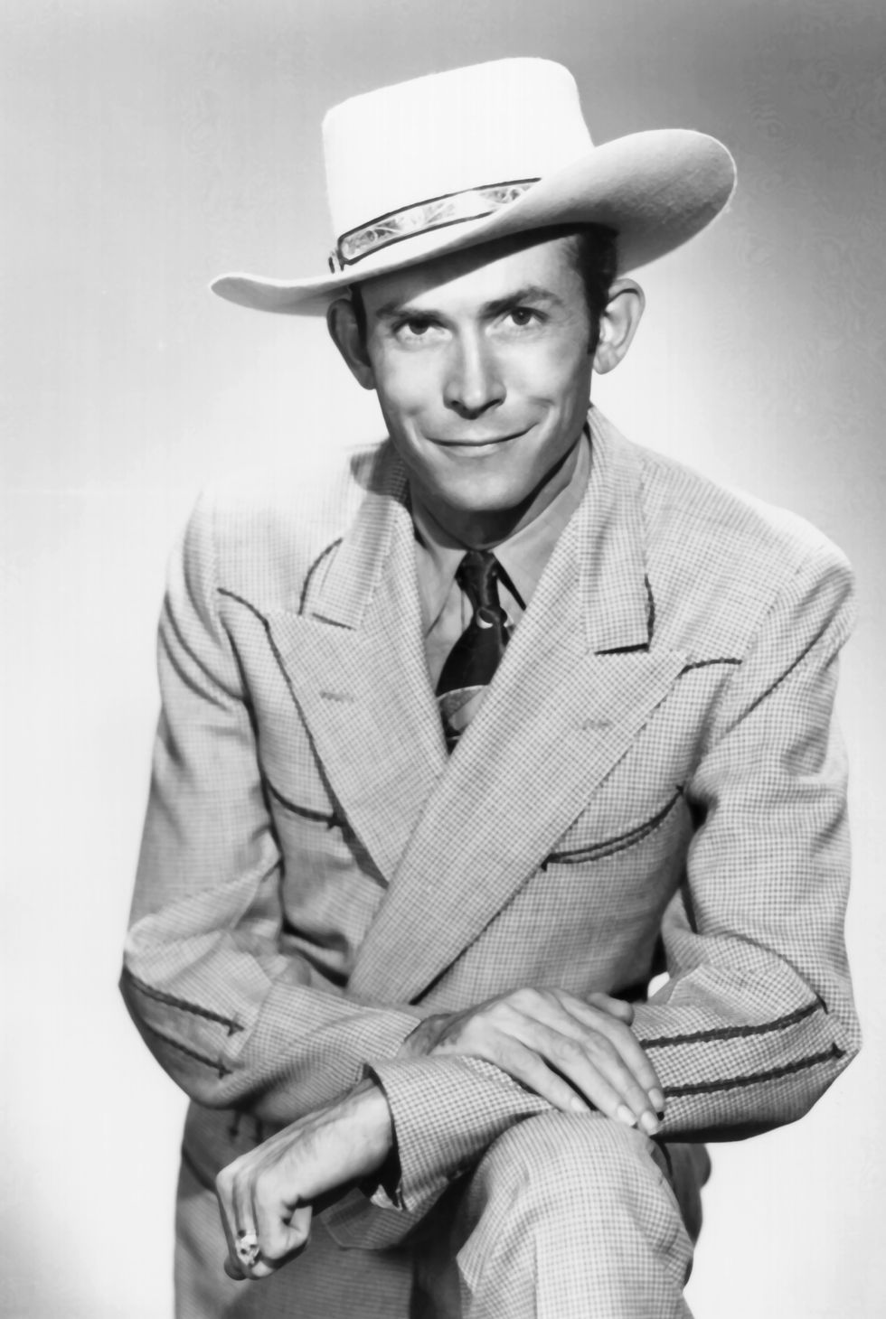 hank williams standing his arms folded on top of his left knee and smiling