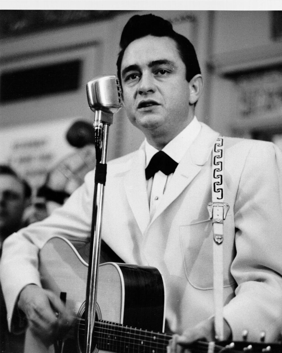 johnny cash playing a guitar and looking toward an audience behind a standing microphone