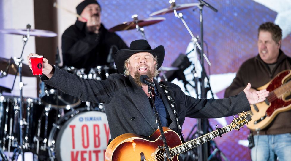 toby keith holding a red solo cup as he plays guitar and sings