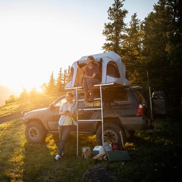 Couple camping, relaxing at SUV rooftop tent in sunny, idyllic field, Alberta, Canada